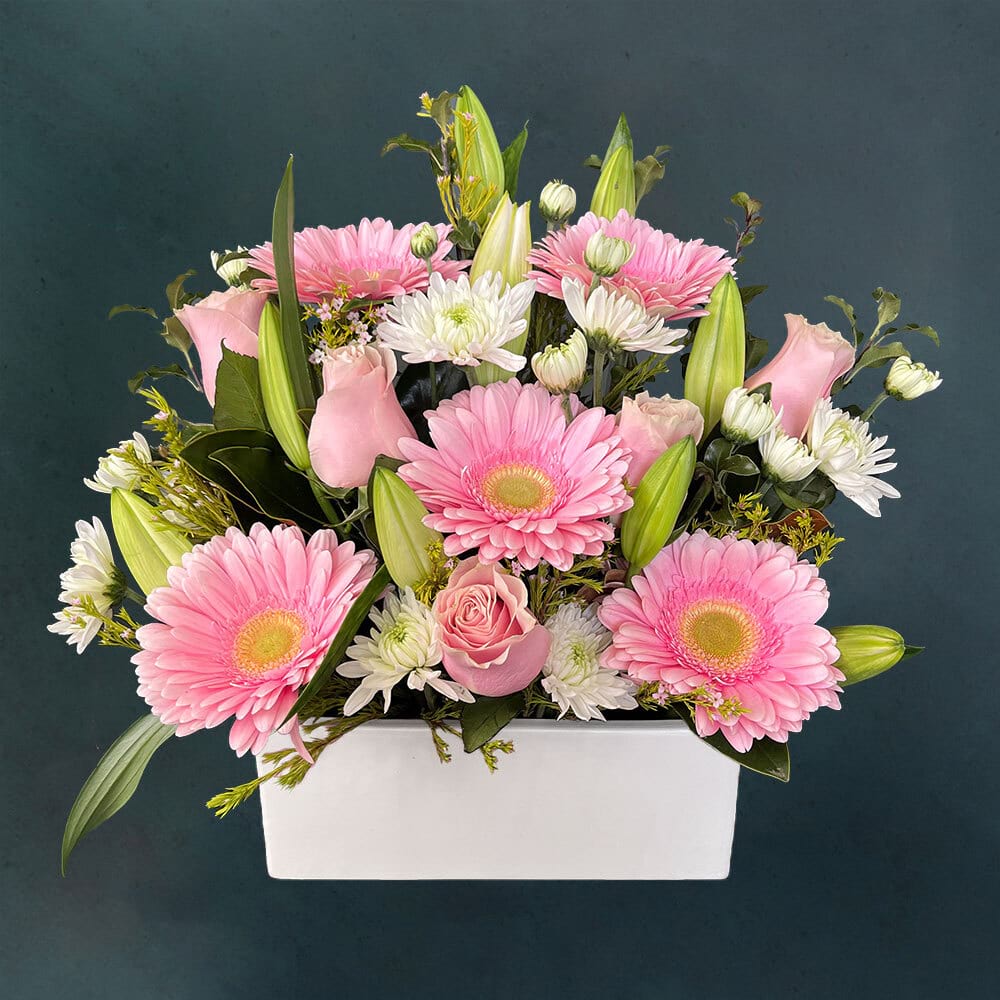 Charming flower arrangement featuring fresh seasonal flowers in soft pink pastel tones presented in a ceramic container