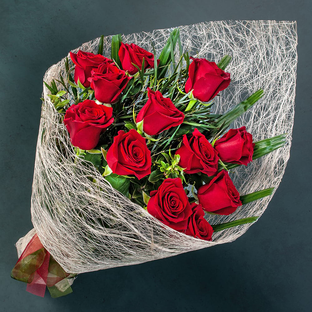 Delightful Dozen bouquet featuring twelve premium Colombian red roses with fresh seasonal foliage beautifully wrapped for delivery